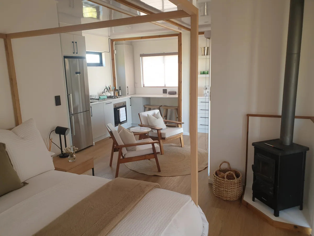 36m² 1-Bedroom Container House — Insulated Standard Configuration — supplier gallery view 6; Container house interior showing a bed in the foreground, wood-burning stove and open-plan kitchen and seating area