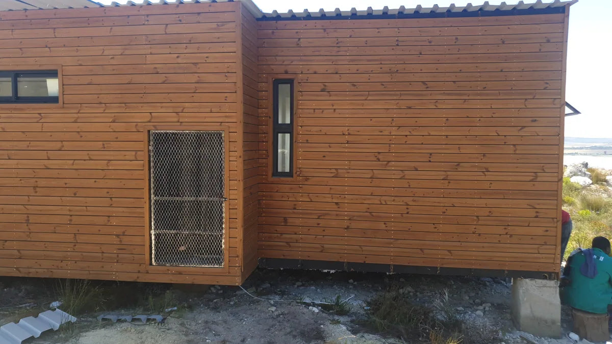94m² 2-Bedroom Container House — Insulated Standard Configuration — supplier gallery view 4; Timber-clad modular home exterior with a security-screened window, with a person partly visible at the edge of the frame
