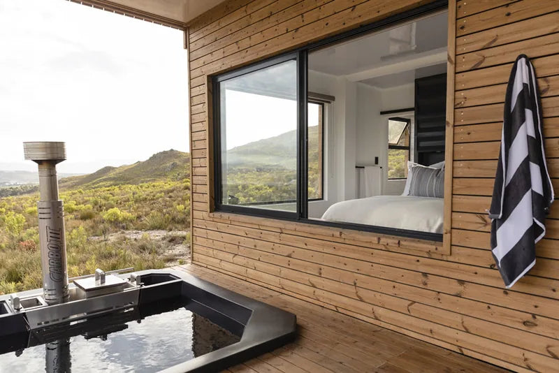 94m² 2-Bedroom Container House — Insulated Standard Configuration — supplier gallery view 5; Outdoor bath on a deck beside a timber-clad home, with a towel hanging by the window and mountains behind