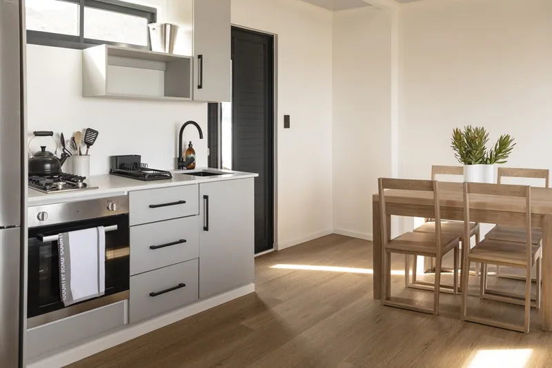 94m² 2-Bedroom Container House — Insulated Standard Configuration — supplier gallery view 8; Kitchen with white cabinets, gas hob, built-in oven and an adjacent timber dining table and chairs