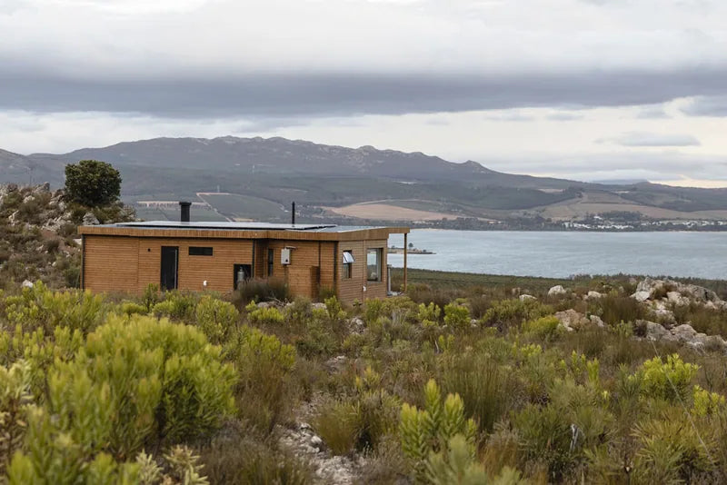 94m² 2-Bedroom Container House — Insulated Standard Configuration — supplier gallery view 3; Timber-clad modular home set in coastal fynbos with a lagoon and mountain range in the background
